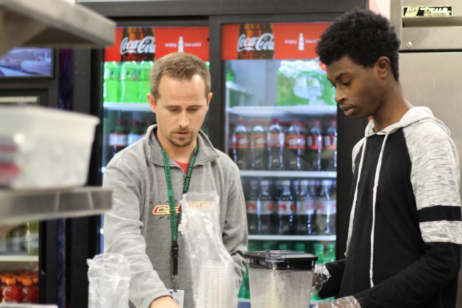At the concession stand, junior Hashim Abu prepares smoothies with ELL teacher Travis Mauzey Nov.16. Abu manages the money raised and paperwork for the smoothie production. Its definitely made me more organized, said Abu. Photo by Autumn Adams